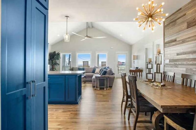 dining space featuring ceiling fan with notable chandelier, high vaulted ceiling, wood finished floors, and wooden walls