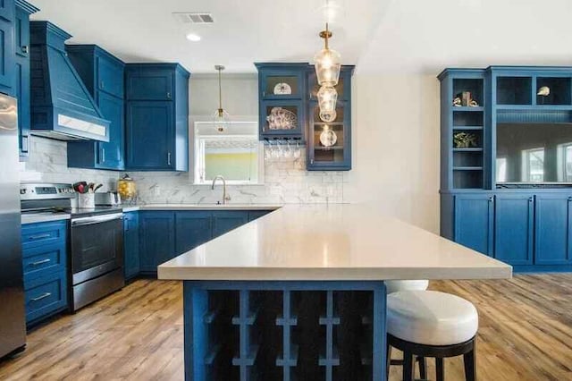 kitchen with appliances with stainless steel finishes, custom exhaust hood, light countertops, blue cabinetry, and a kitchen bar