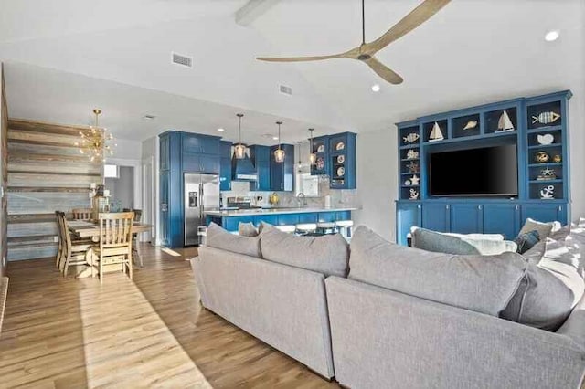 living room featuring vaulted ceiling with beams, ceiling fan with notable chandelier, wood finished floors, and visible vents