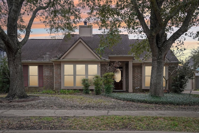 view of front facade with a shingled roof, a chimney, and brick siding