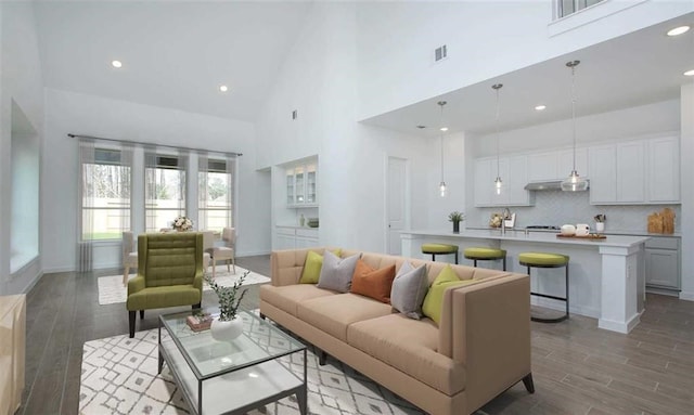 living area featuring baseboards, visible vents, a towering ceiling, light wood-style floors, and recessed lighting