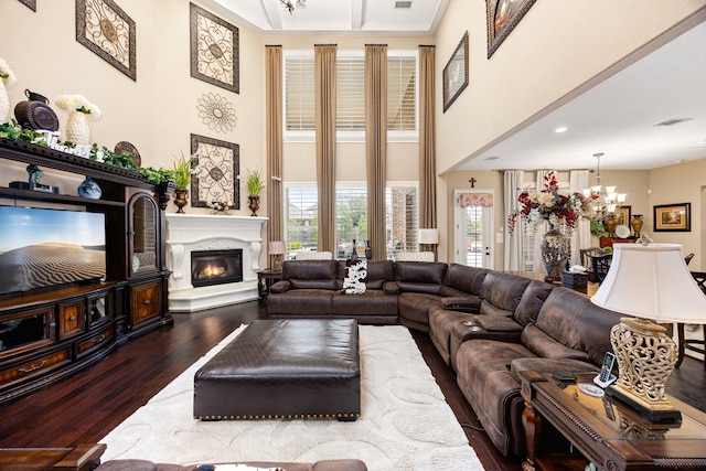 living area with a chandelier, a high ceiling, wood finished floors, visible vents, and a glass covered fireplace