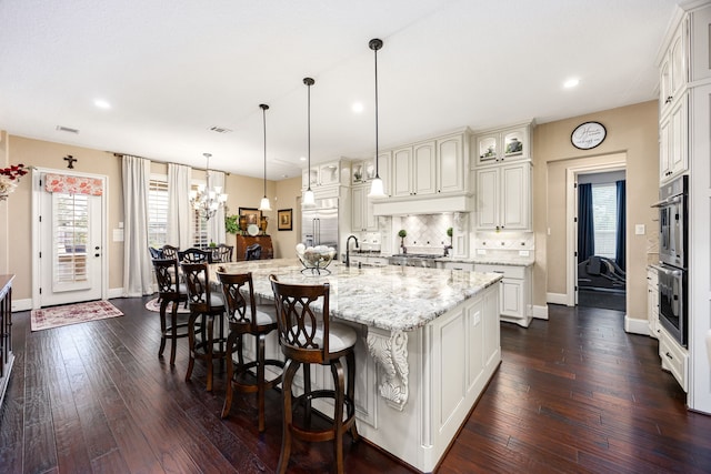 kitchen with a spacious island, appliances with stainless steel finishes, glass insert cabinets, light stone counters, and decorative light fixtures