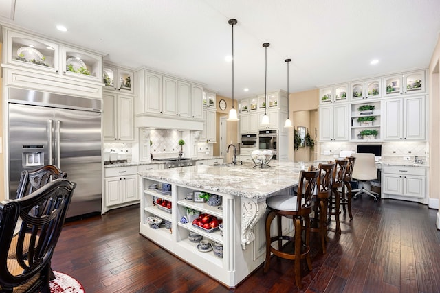 kitchen featuring open shelves, stainless steel appliances, hanging light fixtures, glass insert cabinets, and a kitchen island with sink