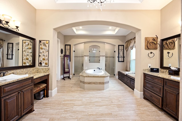 bathroom with a shower stall, a tray ceiling, two vanities, and a sink