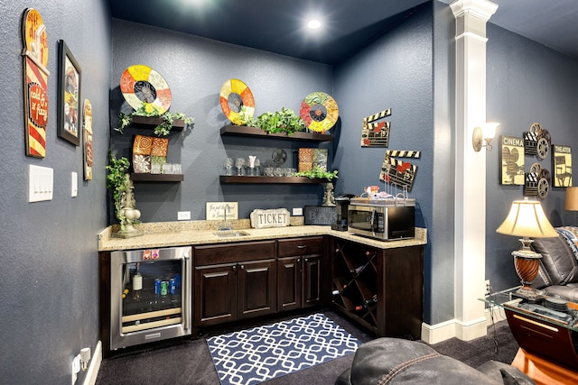 bar with wine cooler, baseboards, a dry bar, stainless steel microwave, and ornate columns