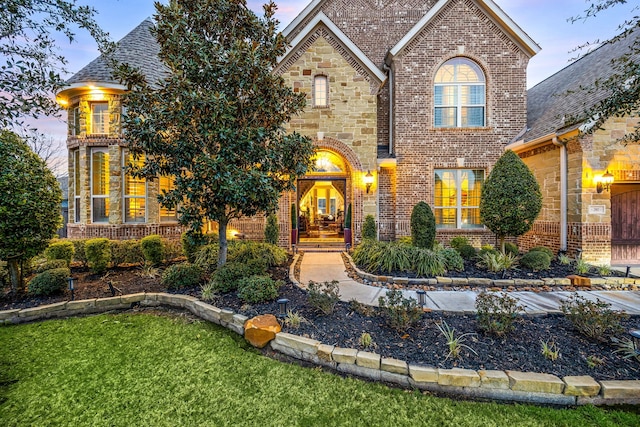 view of front of house featuring stone siding, brick siding, and roof with shingles