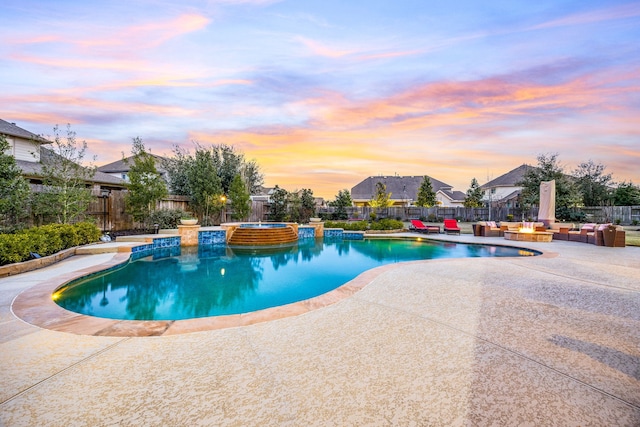 pool at dusk featuring a pool with connected hot tub, fence, and a patio