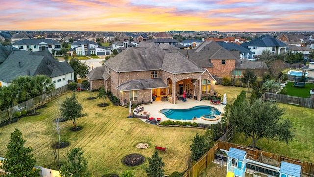 pool at dusk with a yard, a pool with connected hot tub, a patio area, a residential view, and a fenced backyard