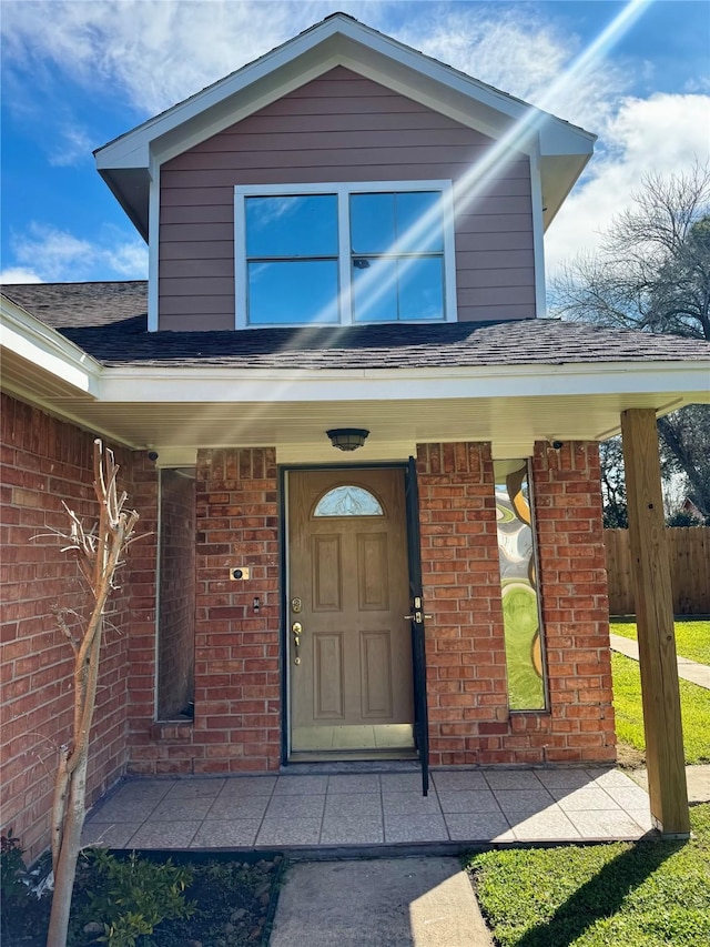 doorway to property featuring a porch, brick siding, and roof with shingles