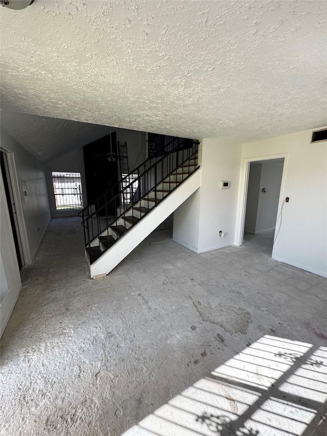 unfurnished living room with a textured ceiling, visible vents, baseboards, stairs, and vaulted ceiling