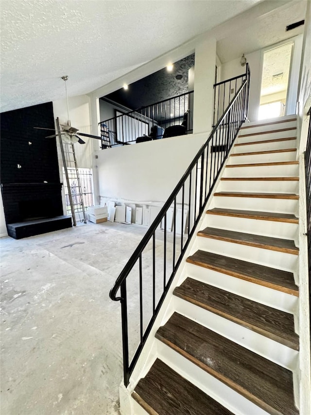 staircase featuring a towering ceiling, ceiling fan, a textured ceiling, and unfinished concrete flooring