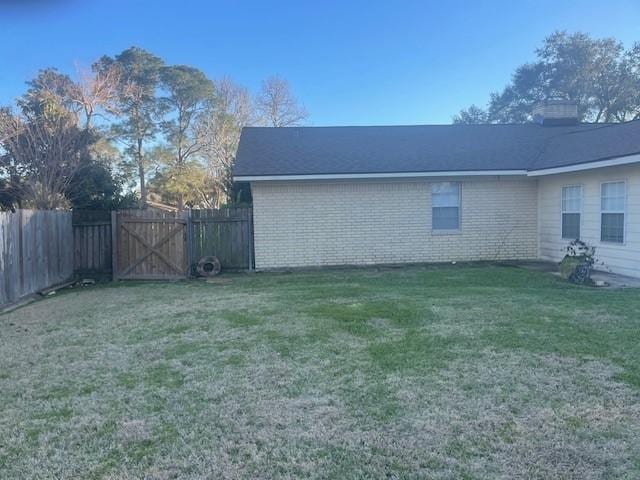 view of home's exterior with a gate, brick siding, fence, and a lawn