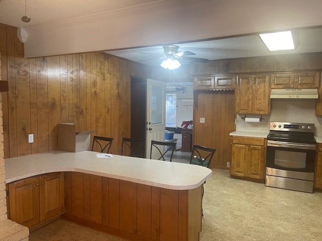 kitchen featuring under cabinet range hood, a peninsula, electric stove, light countertops, and brown cabinets