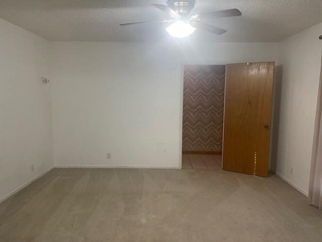 empty room with light carpet, ceiling fan, a textured ceiling, and baseboards