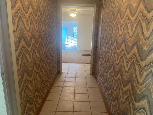 corridor with wallpapered walls, light carpet, baseboards, and light tile patterned floors