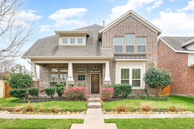 craftsman-style house with roof with shingles, a front yard, and brick siding