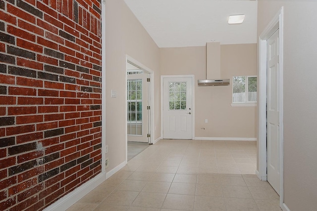 interior space featuring light tile patterned floors, brick wall, and baseboards