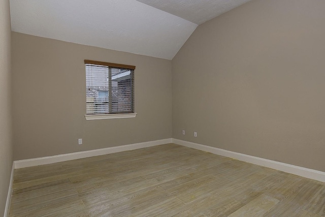 unfurnished room with lofted ceiling, light wood finished floors, and baseboards