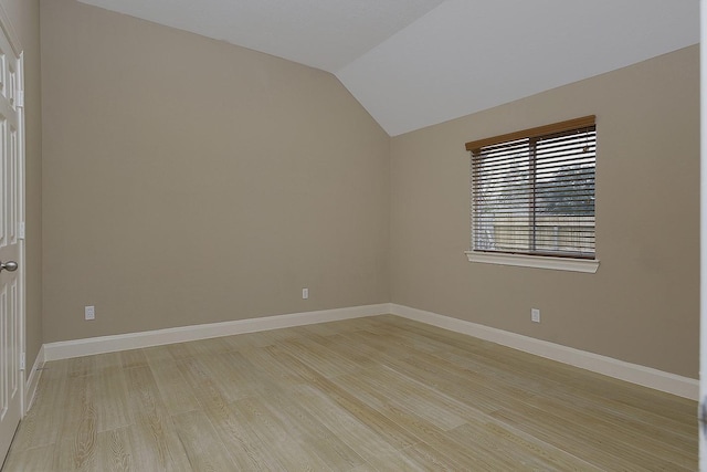 spare room with light wood-type flooring, baseboards, and vaulted ceiling