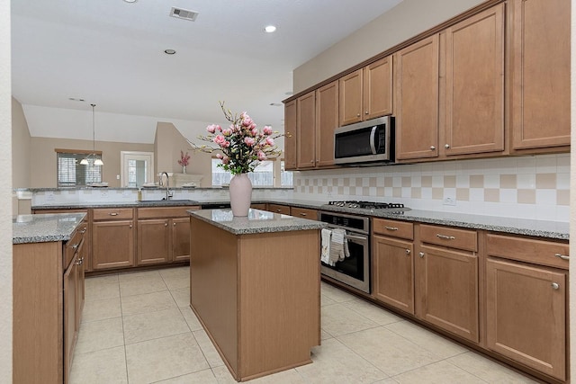 kitchen with light stone countertops, stainless steel appliances, a peninsula, a sink, and a center island