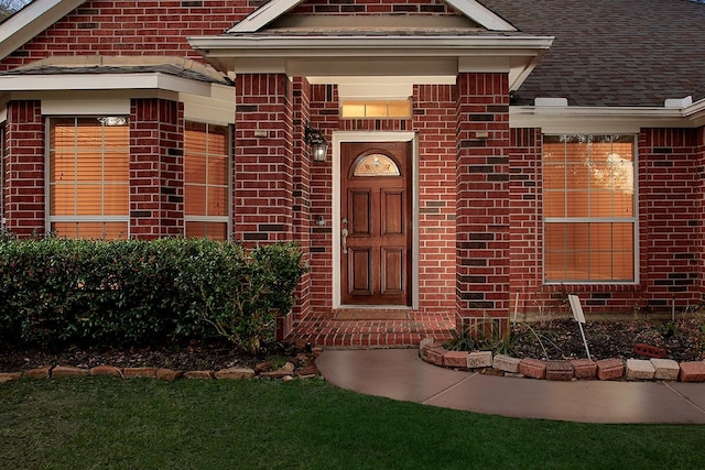 view of exterior entry featuring brick siding and roof with shingles