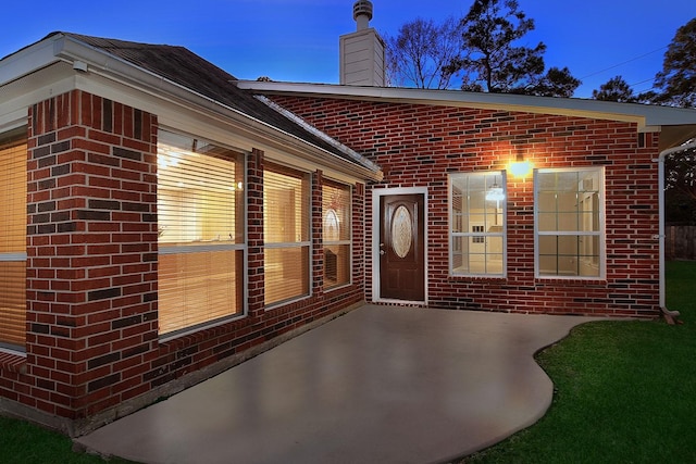 exterior entry at dusk with brick siding, a patio, and a chimney