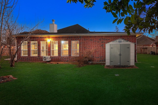 back of house at dusk featuring brick siding, a yard, fence, a shed, and an outdoor structure