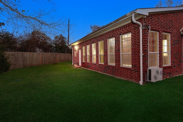 view of side of property featuring ac unit, brick siding, fence, and a lawn