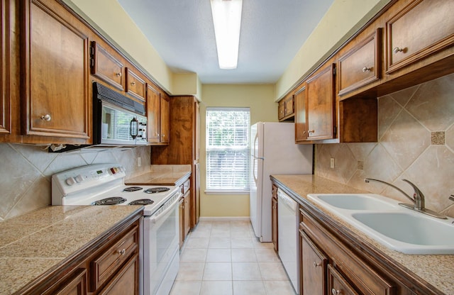 kitchen with tile countertops, backsplash, brown cabinetry, a sink, and white appliances