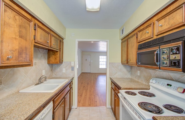 kitchen featuring white appliances, visible vents, brown cabinetry, and a sink