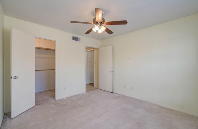 unfurnished bedroom featuring visible vents, a ceiling fan, light colored carpet, a walk in closet, and a closet