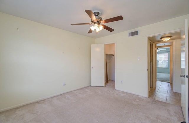 unfurnished bedroom featuring light carpet, a ceiling fan, visible vents, baseboards, and a spacious closet