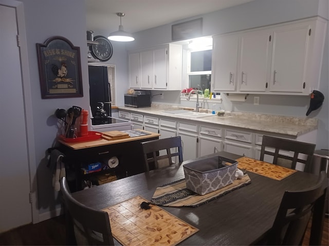 kitchen featuring hanging light fixtures, white cabinetry, light countertops, and a sink