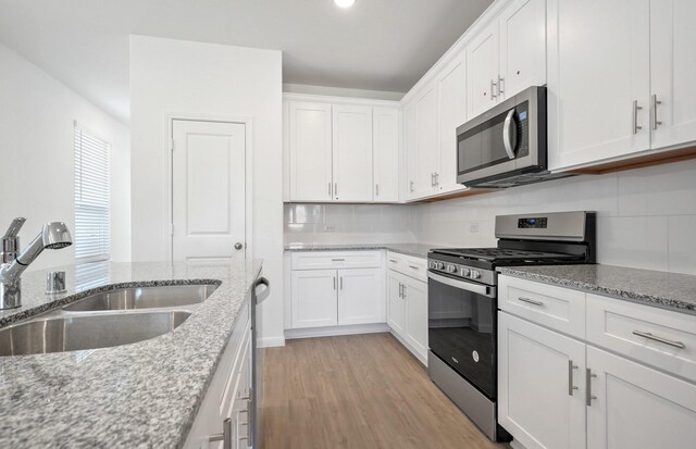 10702 Sora Dr, Willis, TX 77378 - kitchen with light wood finished floors, a sink, stainless steel appliances, white cabinets, and backsplash