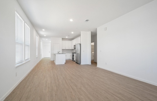 10702 Sora Dr, Willis, TX 77378 - unfurnished living room with visible vents, baseboards, light wood finished floors, recessed lighting, and a sink