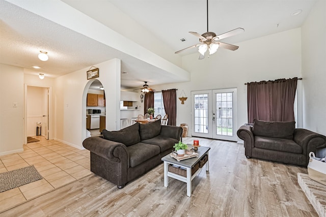 living area with arched walkways, french doors, a textured ceiling, light wood-type flooring, and baseboards