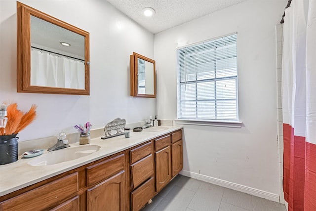 bathroom with double vanity, a textured ceiling, baseboards, and a sink