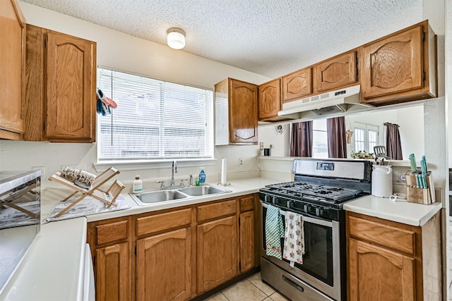 kitchen featuring under cabinet range hood, a sink, light countertops, brown cabinetry, and stainless steel range with gas stovetop