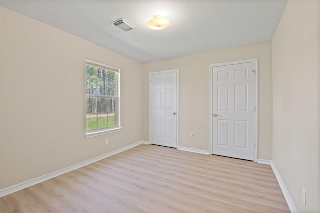 unfurnished bedroom with a textured ceiling, light wood-type flooring, visible vents, and baseboards