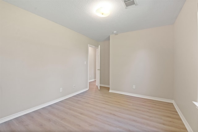 unfurnished room with light wood finished floors, baseboards, visible vents, and a textured ceiling