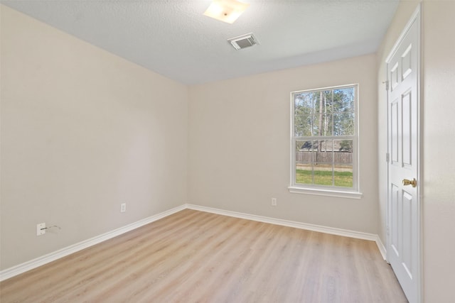 spare room with light wood-type flooring, baseboards, visible vents, and a textured ceiling