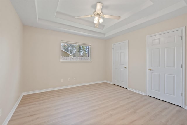 unfurnished bedroom featuring a ceiling fan, light wood-style flooring, a tray ceiling, and baseboards