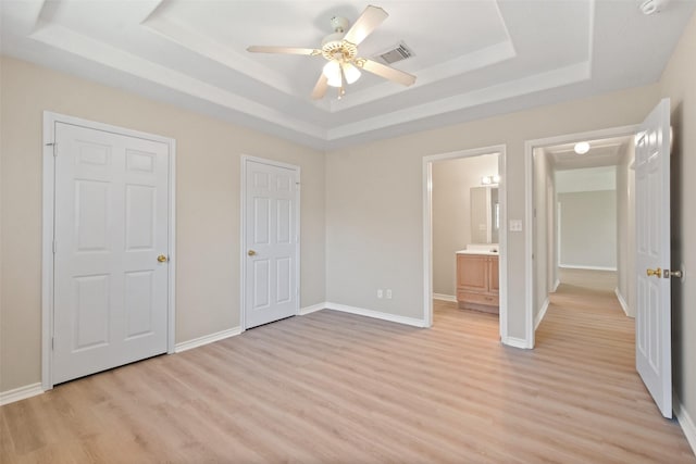 unfurnished bedroom featuring light wood-type flooring, a tray ceiling, visible vents, and baseboards