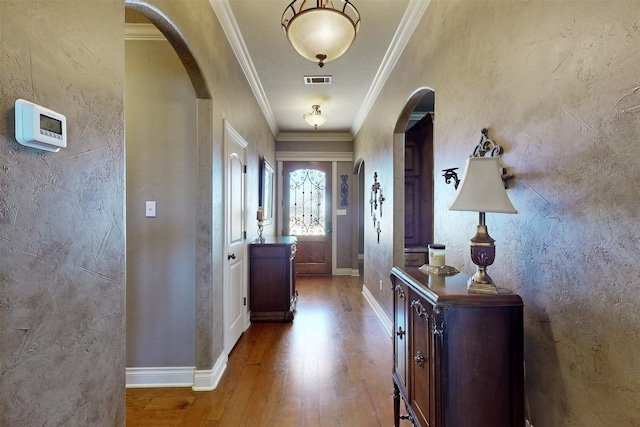 doorway featuring visible vents, arched walkways, wood finished floors, and ornamental molding