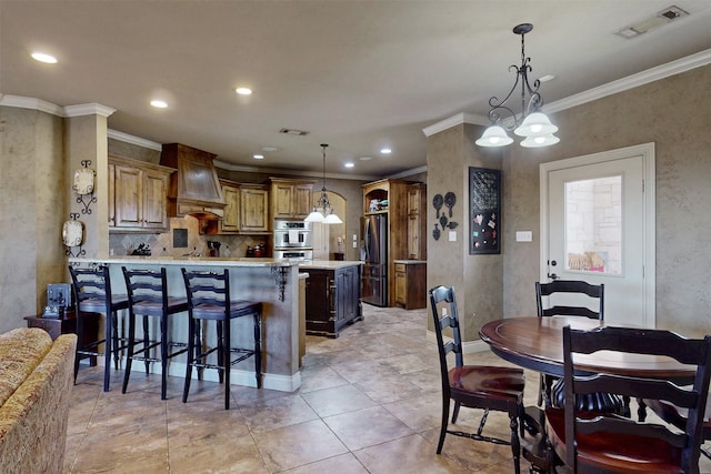 kitchen featuring a breakfast bar area, visible vents, appliances with stainless steel finishes, custom exhaust hood, and decorative light fixtures