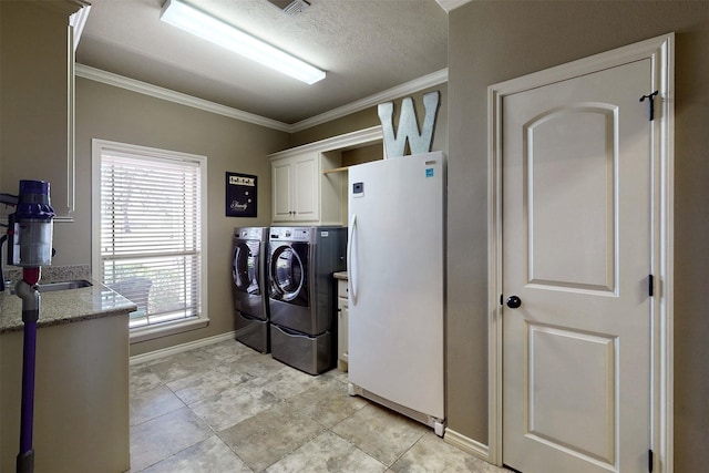 washroom featuring a textured ceiling, baseboards, washer and dryer, ornamental molding, and cabinet space