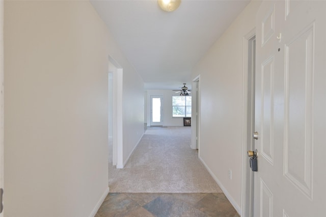 corridor with stone finish floor, baseboards, and light colored carpet