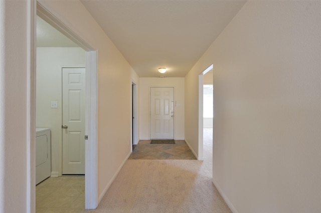 hall with baseboards, washer / clothes dryer, and light colored carpet