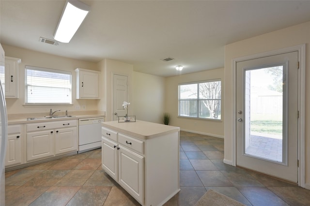 kitchen with white dishwasher, a sink, a kitchen island, white cabinets, and light countertops